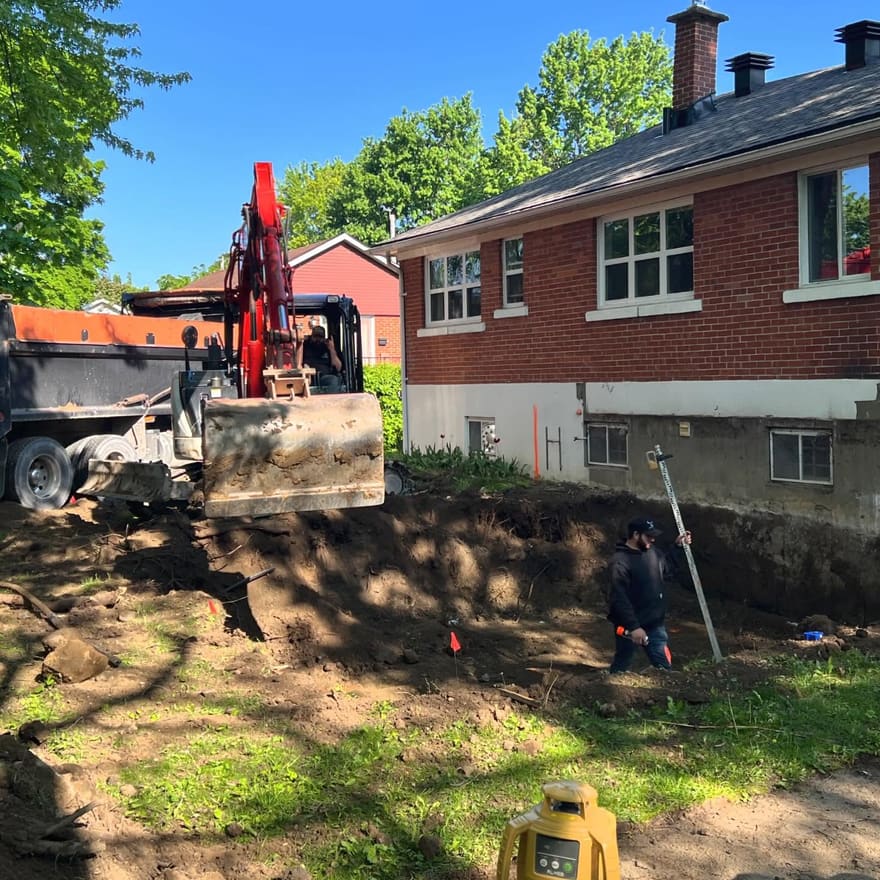 Excavatrice creusant la fondation d’un agrandissement derrière un bungalow en brique